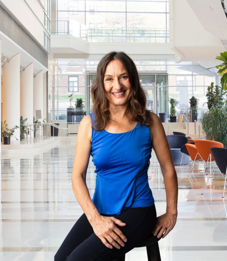 Martina in blauem Top und schwarzer Hose sitzt im Foyer eines schicken Bürogebäudes